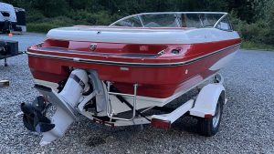 Boat with red and white colors parked on gravel.
