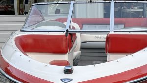 A red and white boat with a seat and a steering wheel, floating on calm waters.